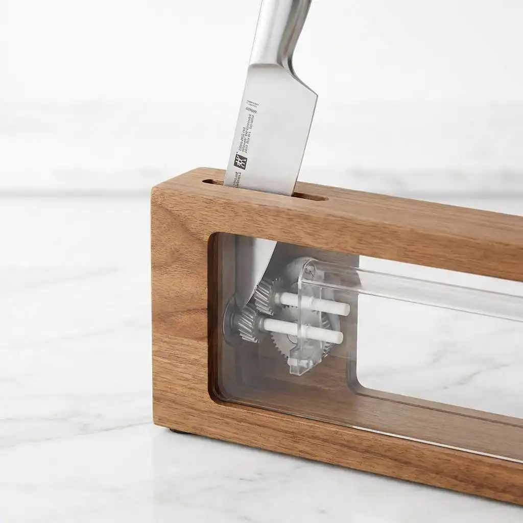 A knife blade entering a self-sharpening block slot on a sterile white marble kitchen counter. A knife blade entering a self-sharpening block slot on a sterile white marble kitchen counter.