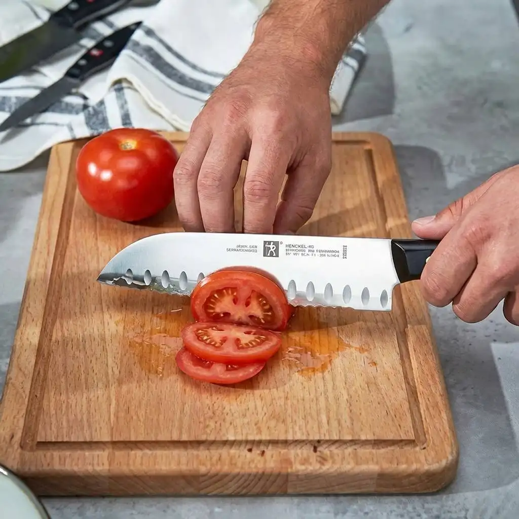 Sharp chef's knife slicing a juicy red tomato on a wooden butcher block in a brightly lit kitchen.