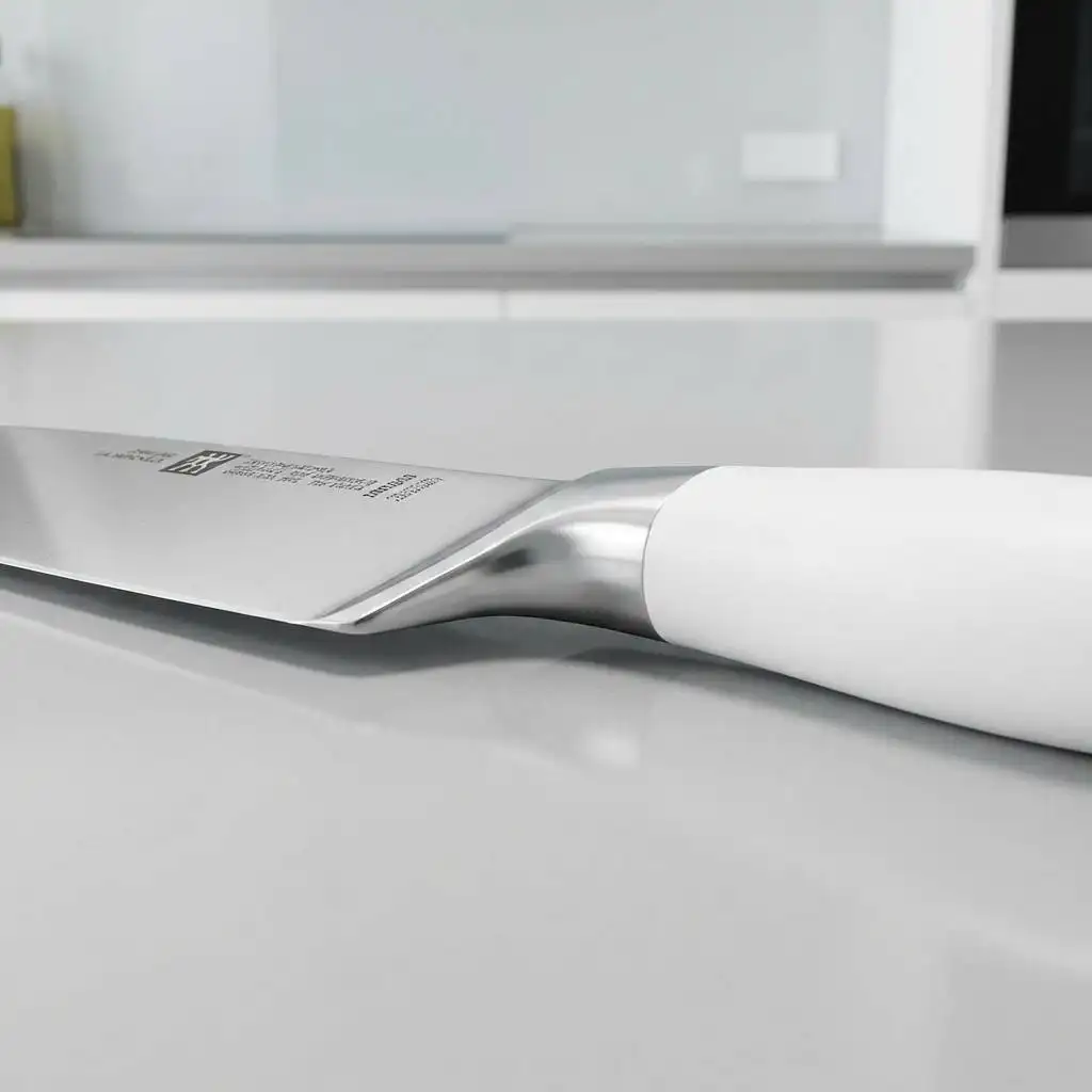 Close-up of a Zwilling kitchen knife's seamless transition between the steel blade and white handle, highlighting the ergonomic, guardless bolster for a comfortable pinch grip. Close-up of a Zwilling kitchen knife's seamless transition between the steel blade and white handle, highlighting the ergonomic, guardless bolster for a comfortable pinch grip.